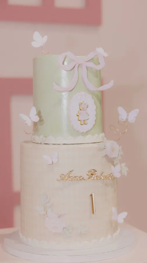 Two-tier custom birthday cake in sage green and gingham buttercream with a sugar bow, butterflies and a gold number one topper