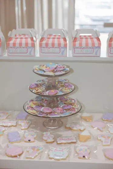 Tiered stand of hand-iced cookies next to striped treat boxes on the dessert table