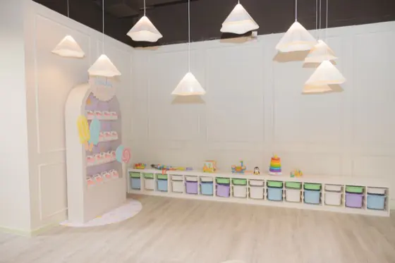 Open event hall at Playville with pendant lights, a pastel candy display and toy storage bins