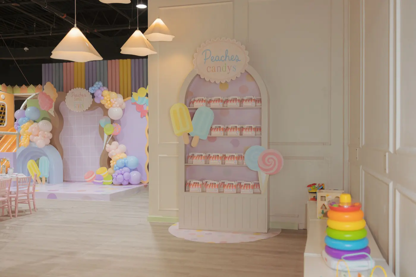 Wide view of the Playville event hall: pendant lights, a candy display wall, party tables and the indoor playground